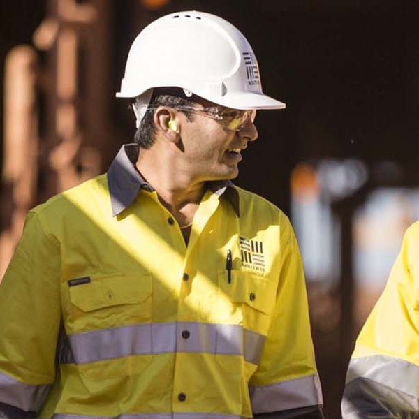 Two workers at our Worsley operation in uniform walking with machinery in the background.